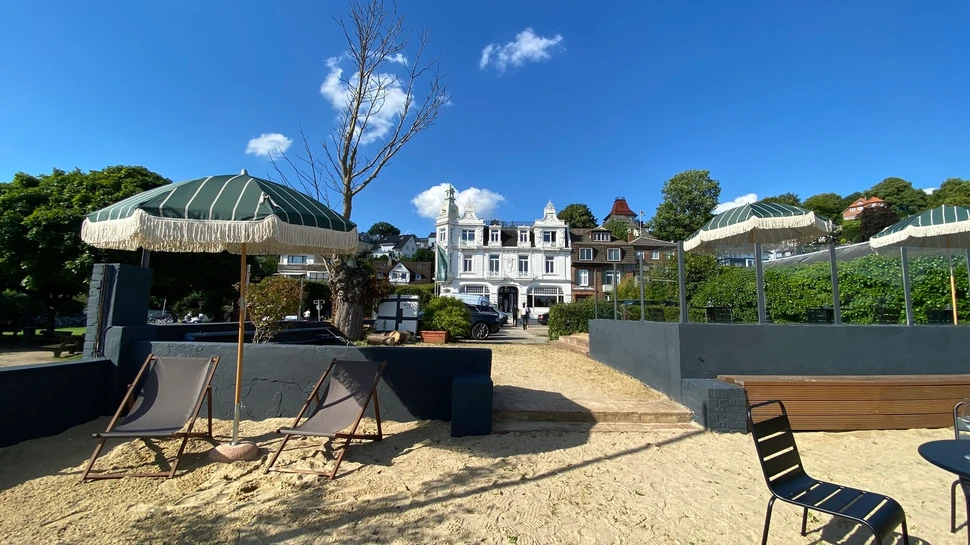 Strandhotel Blankenese mit Sandstrand, grünen Sonnenschirmen und Liegestühlen vor historischer Villa