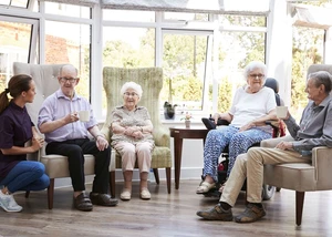 Eine Gruppe von vier Senioren und Seniorinnen und einer Pflegekraft sitzen gemütlich in Stühlen