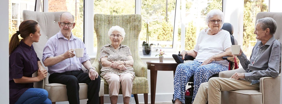 Eine Gruppe von vier Senioren und Seniorinnen und einer Pflegekraft sitzen gemütlich in Stühlen