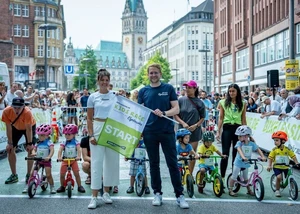 Kinder auf Laufrädern und zwei Erwachsene mit Start-Flagge