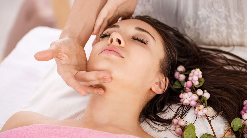 eine Frau erhält eine Gesichtsmassage, neben ihr liegen Blumen