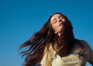Sängerin Sigrid steht mit wehenden Haaren vor blauem Himmel