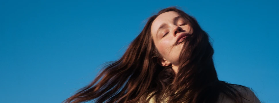 Sängerin Sigrid steht mit wehenden Haaren vor blauem Himmel