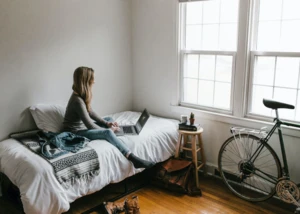 junge Frau sitzt mit Laptop auf einem Bett
