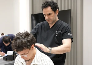 Mann sitzt auf einem Friseurstuhl und lässt von einem anderen beraten