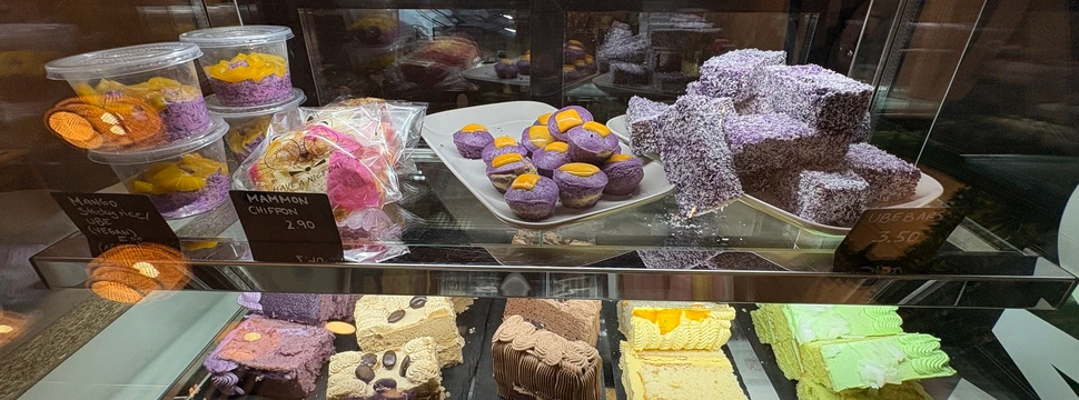 Diverse süße Teilchen, teils in Lila gefärbt in einer Glasvitrine