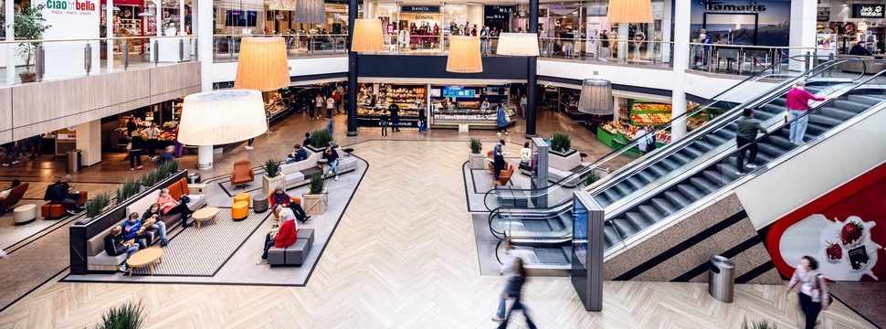 Blick in ein Einkaufszentrum mit großem Glasdach und Rolltreppen