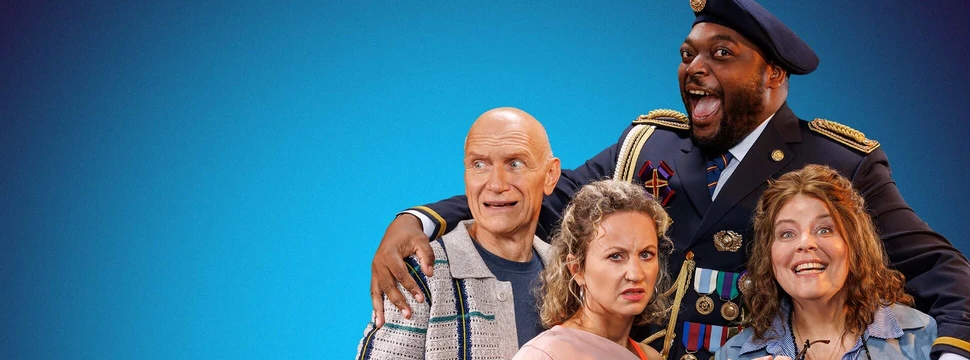 Ensemble der Komödie "Der 50-Dollar-Diktator" im Schmidt Theater Hamburg: vier Schauspieler in Kostümen vor blauem Hintergrund, darunter ein Mann in Militäruniform mit Baskenmütze und eine Frau im blauen Anzug