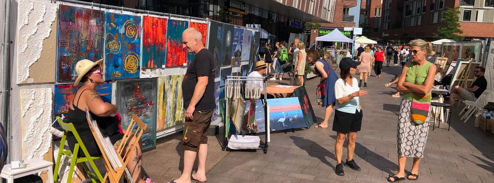 "Hamburg zeigt Kunst" Mehrere Menschen spazieren an Gemälden am Überseeboulevard vorbei.