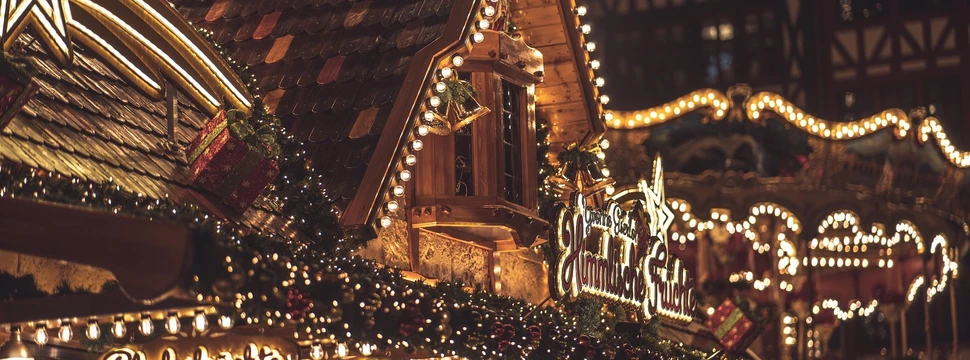 Festlich beleuchtete Weihnachtsmarktstände aus Holz mit Lichterketten und Schildern für Süßwaren