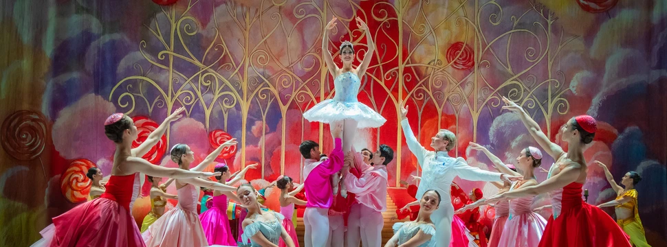 Mehrere Balletttänzer tanzen auf einer bunten und imposanten Bühne.