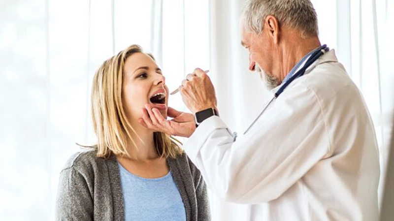 Ein Arzt führt eine HNO-Untersuchung bei einer Patientin durch Arzt mit Stethoskop untersucht den Hals einer blonde Patientin mit einem medizinischen Instrument