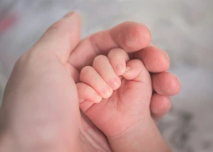 Eine weibliche Hand umschließt die Hand eines Neugeborenen