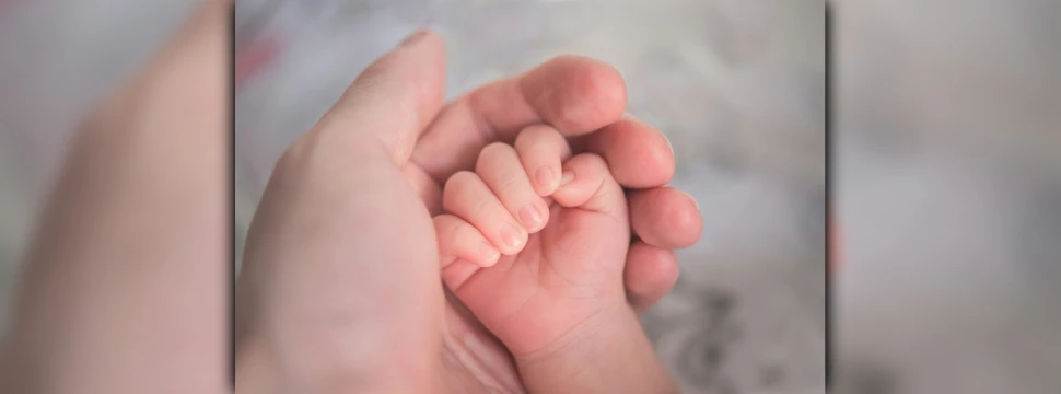 Eine weibliche Hand umschließt die Hand eines Neugeborenen