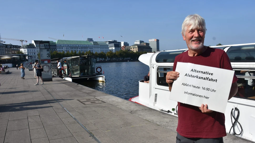 Mann mit einem Schild in der Hand vor einem Schiff auf der Alster