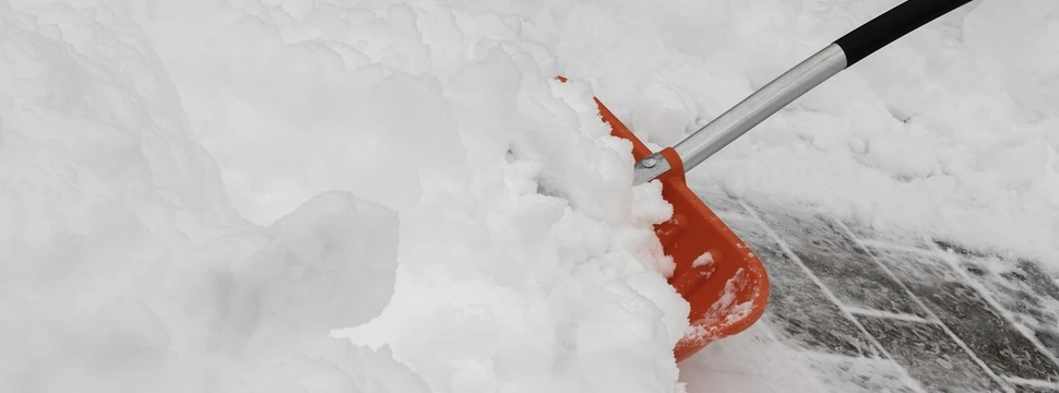 Eine rote Schneeschaufel räumt frischen Schnee von einem Gehweg, um die Fläche sicher und zugänglich zu machen.