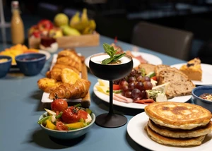 Reichhaltig gedeckter Brunch-Tisch mit Pancakes, Croissants, Käse-Wurst-Platte und Cocktail im nordischen Stil