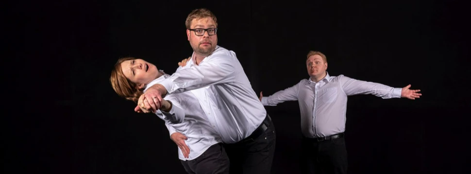 Drei Improvisationsschauspieler in weißen Hemden und dunklen Hosen bei einer dynamischen Theaterszene.