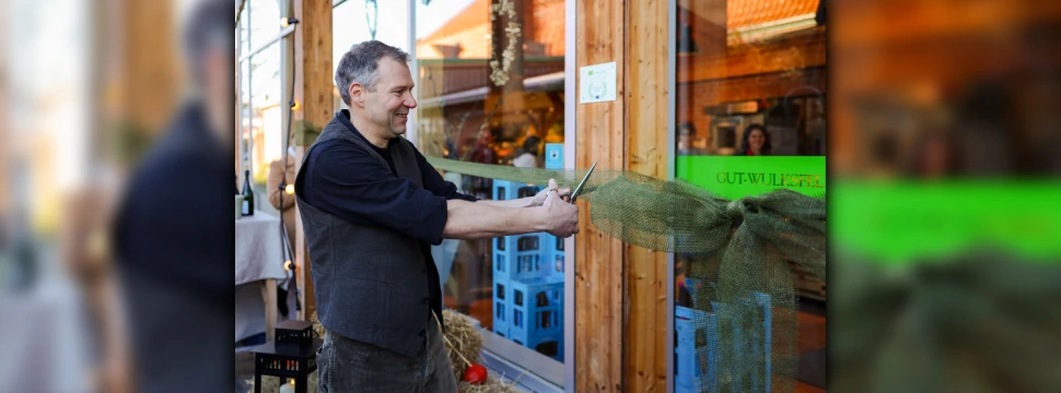 Ein Mann mittleren Alters schneidet mit einer Schere eine Schleife für eine Wiedereröffnung eines Ladens durch