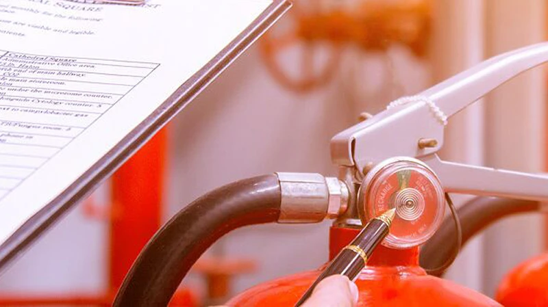 Brandschutz: Ein Feuerlöscher steht bereit für den Ernstfall Roter Feuerlöscher mit Druckanzeige und Schlauch, dahinter verschwommen Sicherheitsdokumente