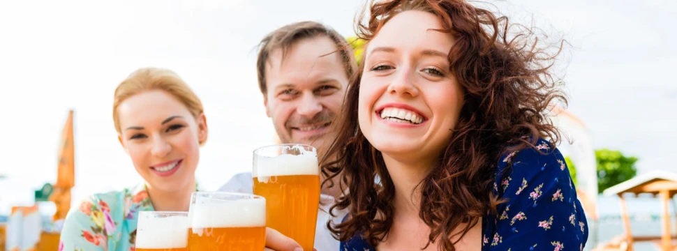 2 Frauen und ein Mann mit Bierglas sitzen in einem Biergarten