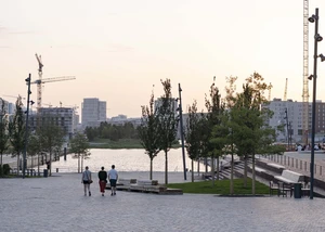 Eine Gruppe von drei Manschen gehen ans Ufer eines Platzes mit Blick auf ein Stadtpanorama
