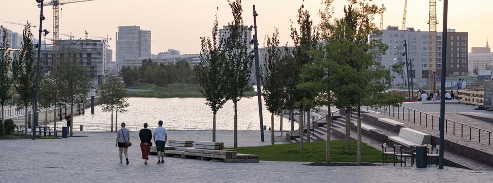 Eine Gruppe von drei Manschen gehen ans Ufer eines Platzes mit Blick auf ein Stadtpanorama
