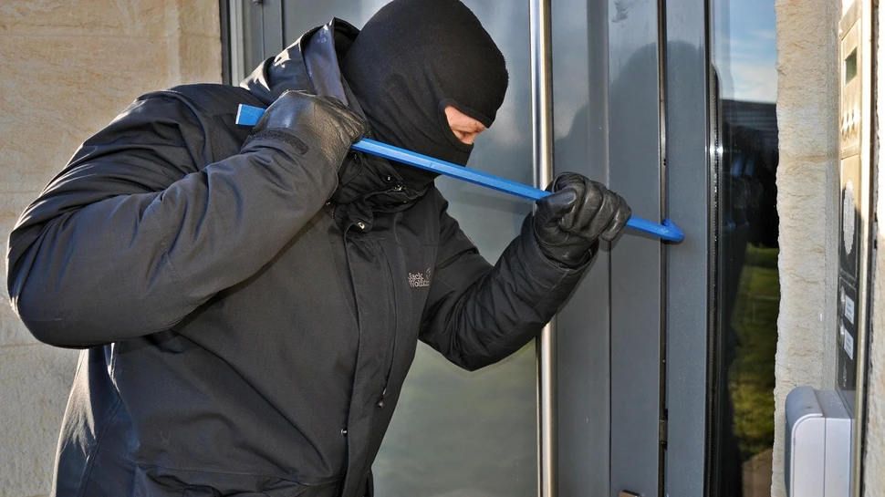 Vermummter Mann mit blauer Eisenstange versucht eine Tür aufzuhebeln