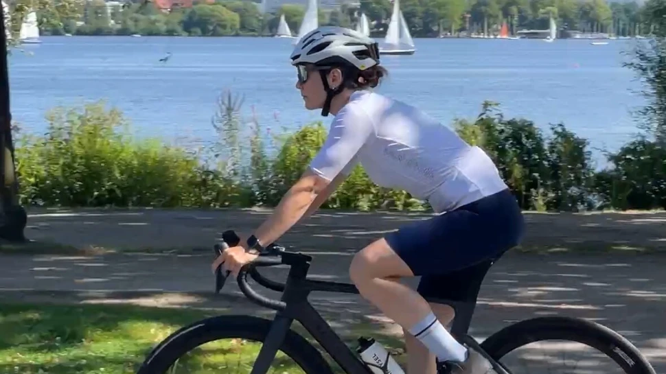 Frau mit weißem Fahrradhelm fährt Rennrad an der Außenalster