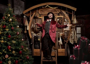 Ein kostümierter Darsteller im Hamburg Dungeon vor einem Weihnachtsbaum und Holzstand mit "Geschenketausch"-Schild.