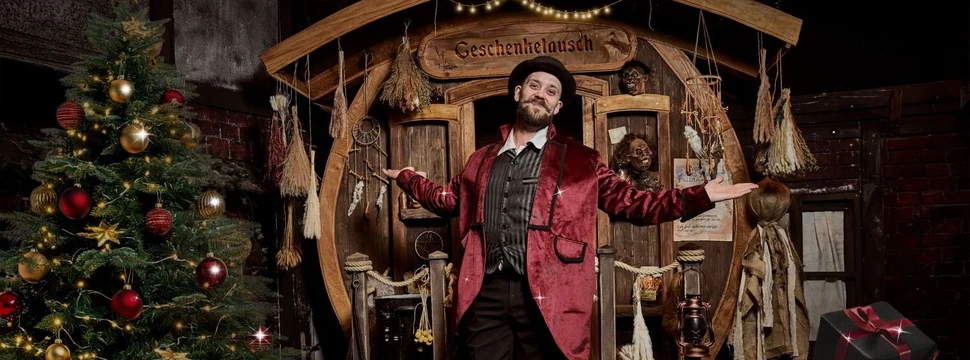 Ein kostümierter Darsteller im Hamburg Dungeon vor einem Weihnachtsbaum und Holzstand mit "Geschenketausch"-Schild.
