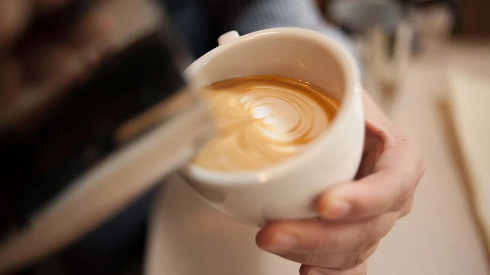 Café au Lait Aus einer silbernen Kanne wird Kaffee in eine weiße Tasse eingeschenkt