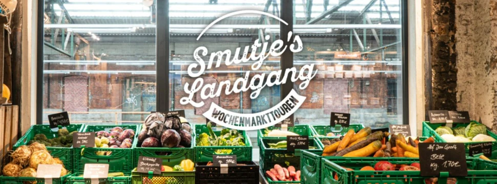 Schaufenster eines Wochenmarkts mit grünen Kisten voller frischem Gemüse und dem Schriftzug "Smutje's Landgang".