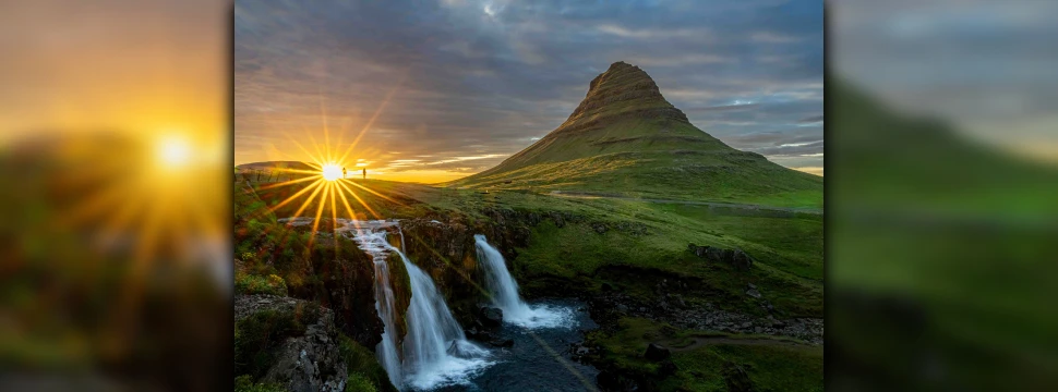 Eine Landschaftaufnahme von einem Berg, davor ist ein Wasserfall, und die Sonne geht gerade am Horizont unter