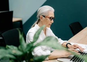 Eine ältere Frau mit Brille arbeitet an einem Laptop