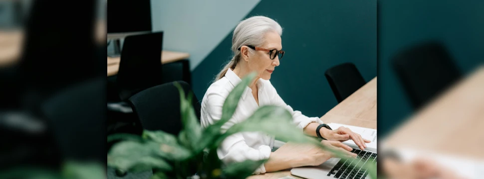 Eine ältere Frau mit Brille arbeitet an einem Laptop