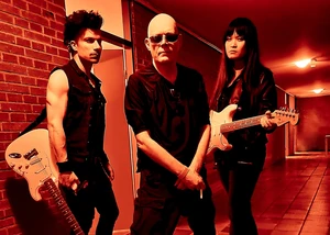 Die Band The Sisters of Mercy posiert in einem rot beleuchteten Flur mit Gitarren.