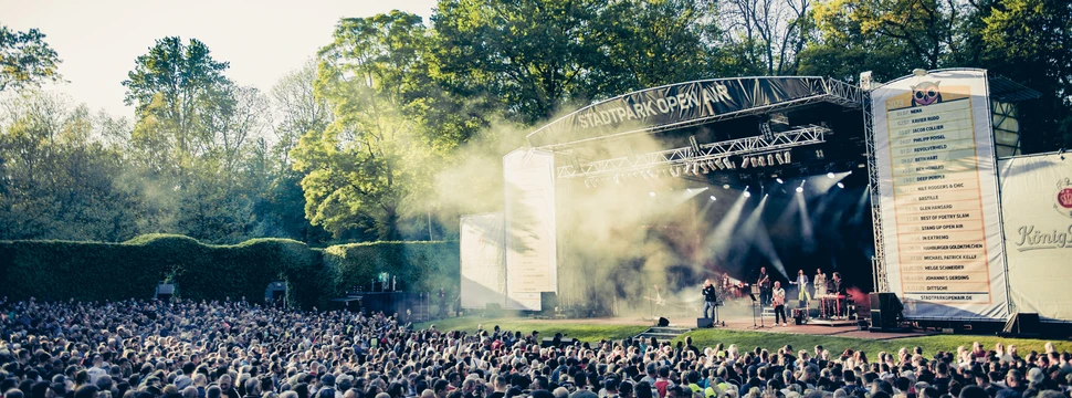 Blick auf eine große Bühne im Stadtpark vor der ein großes Publikum sitzt.