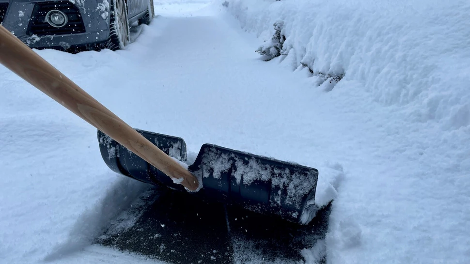 schwarzer Schneeschieber mit Holzgriff im Schnee