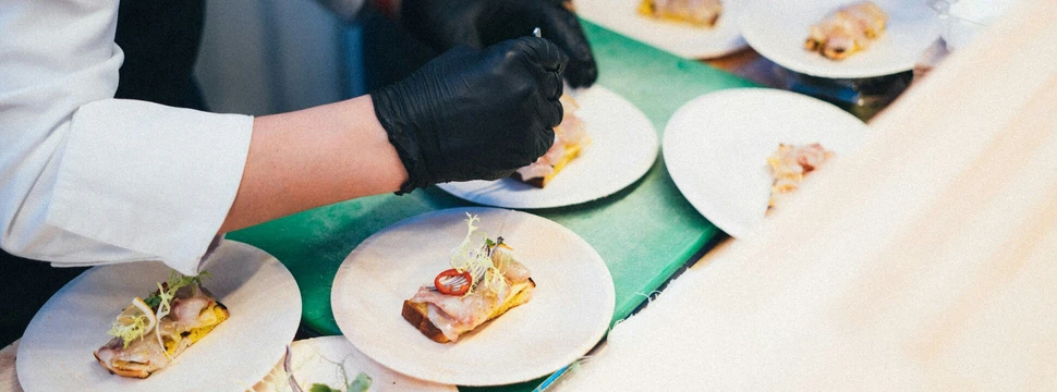 Köche richten kleine Vorspeisen auf weißen Tellern in einer Küche an.