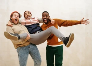 Zwei junge Männer heben einen dritten Mann lachend hoch