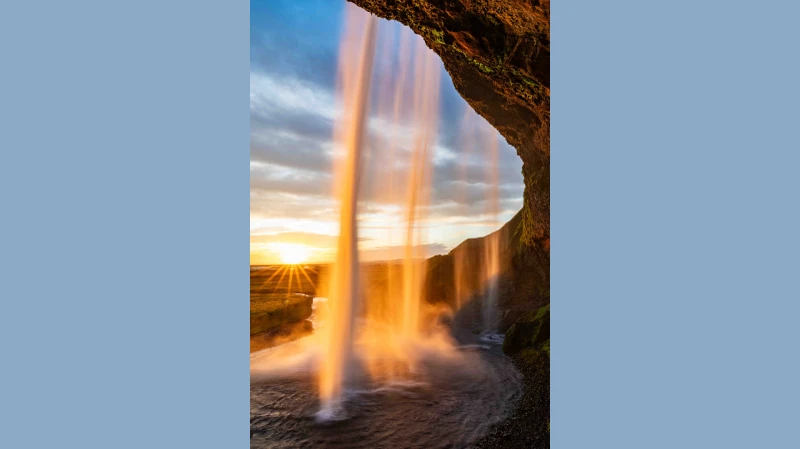 Eine Aufnahme von einem Wasserfall, dahinter geht die Sonne unter