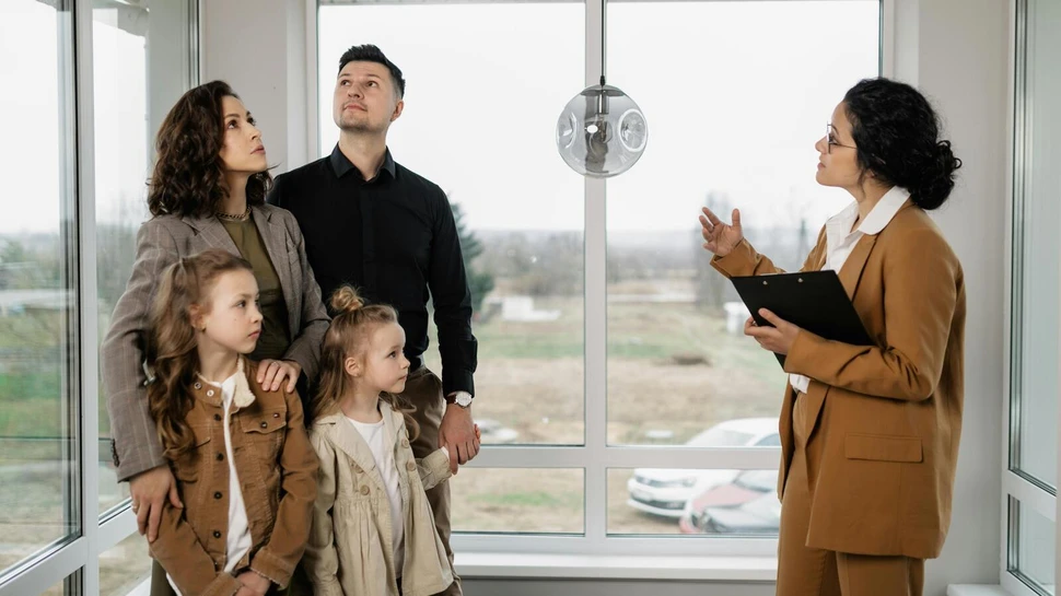 Eine Immobilienmaklerin präsentiert einer Familie mit zwei Mädchen eine Immobilie