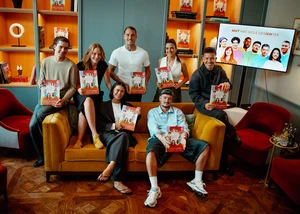 acht Personen sitzen auf einem Sofa und präsentieren ein Kinderbuch