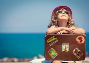 Ein Mädchen mit Sonnenbrille, Sonnenhut und Koffer