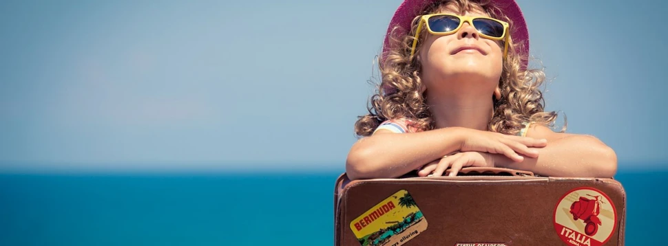 Ein Mädchen mit Sonnenbrille, Sonnenhut und Koffer