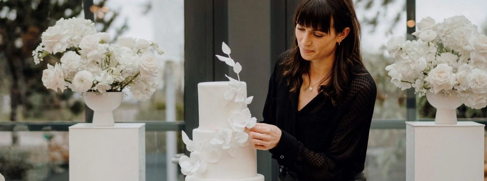 Hochzeitstorte von AURA Tortendesign Eine Frau dekoriert eine weiße Hochzeitstorte