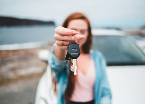 Frau präsentiert Autoschlüssel. Der Schlüssel ist im Fokus.