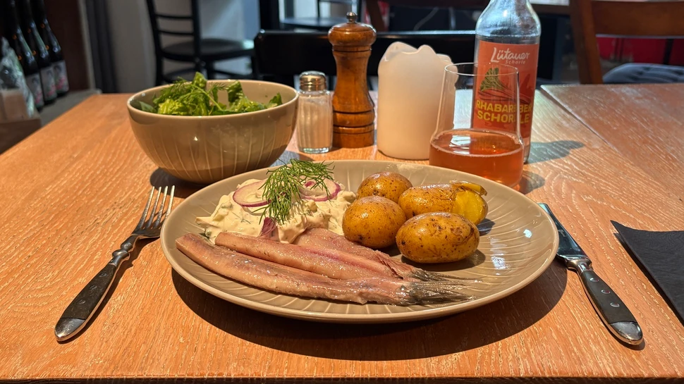 Teller mit Matjes, Pellkartoffeln, Sauce, Schüssel mit grünem Salat und Getränk