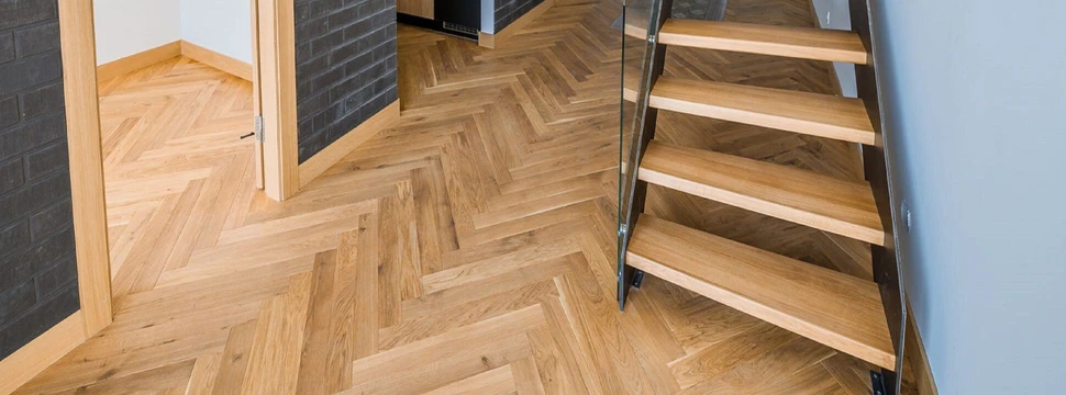 ein Flur mit Fischgrät Parkettboden und einer Holztreppe